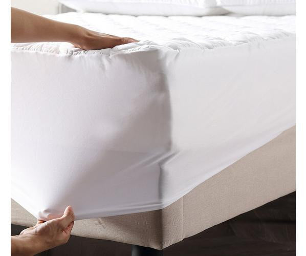 Hands are shown fitting the BRIT DIAMOND Extra Deep 100% Waterproof Quilted Mattress Protector over a mattress on a beige-based bed.