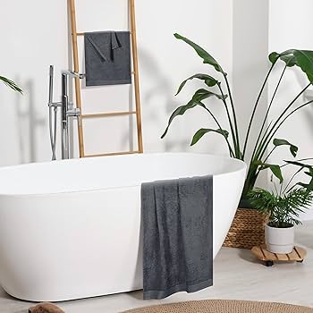 A modern bathroom featuring BRIT DIAMOND’s 100% cotton bath sheets—soft, absorbent large towels in multiple colors—displayed on a ladder rack, with green potted plants and a woven basket on a light floor for quick-drying comfort.