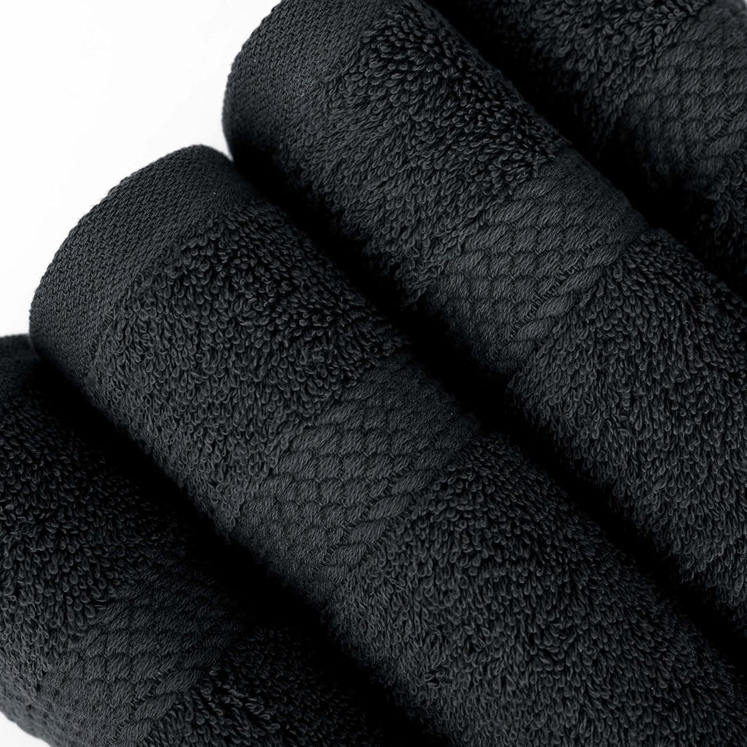 Four BRIT DIAMOND black bath towels, made of 100% cotton with a textured pattern, from the Soft & Absorbent Bath Towels Pack of 4, are neatly rolled and arranged side by side on a white surface.