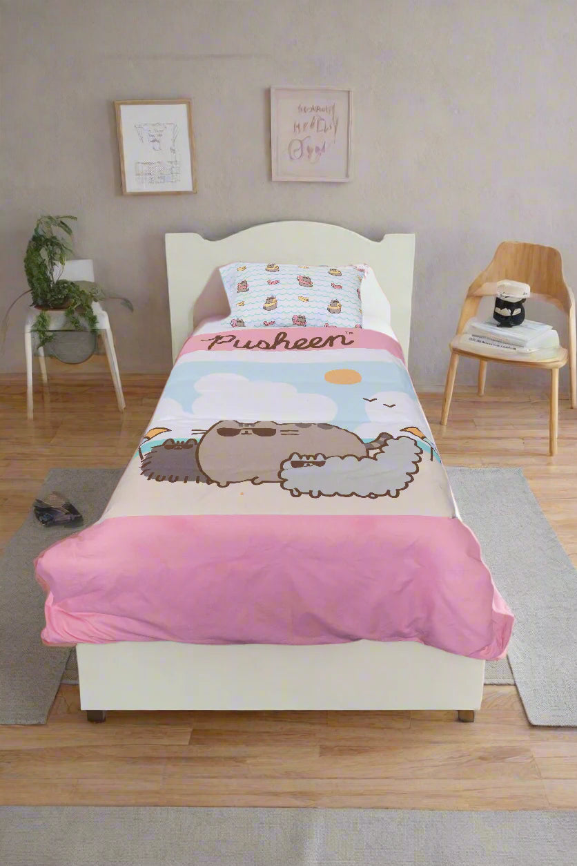 A single bed with the BRIT DIAMOND Kids Pusheen Reversible Duvet Cover Set sits between two nightstands with lamps, against a pink and white wall, in a room with wooden flooring.