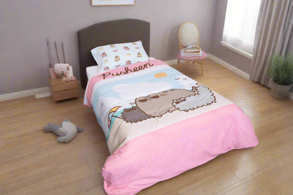 A neatly made single bed features the BRIT DIAMOND Kids Pusheen Reversible Duvet Cover Set – Cute & Cosy Double-Sided Bedding, set against white paneled walls with a green potted plant in the corner on dark blue carpet.