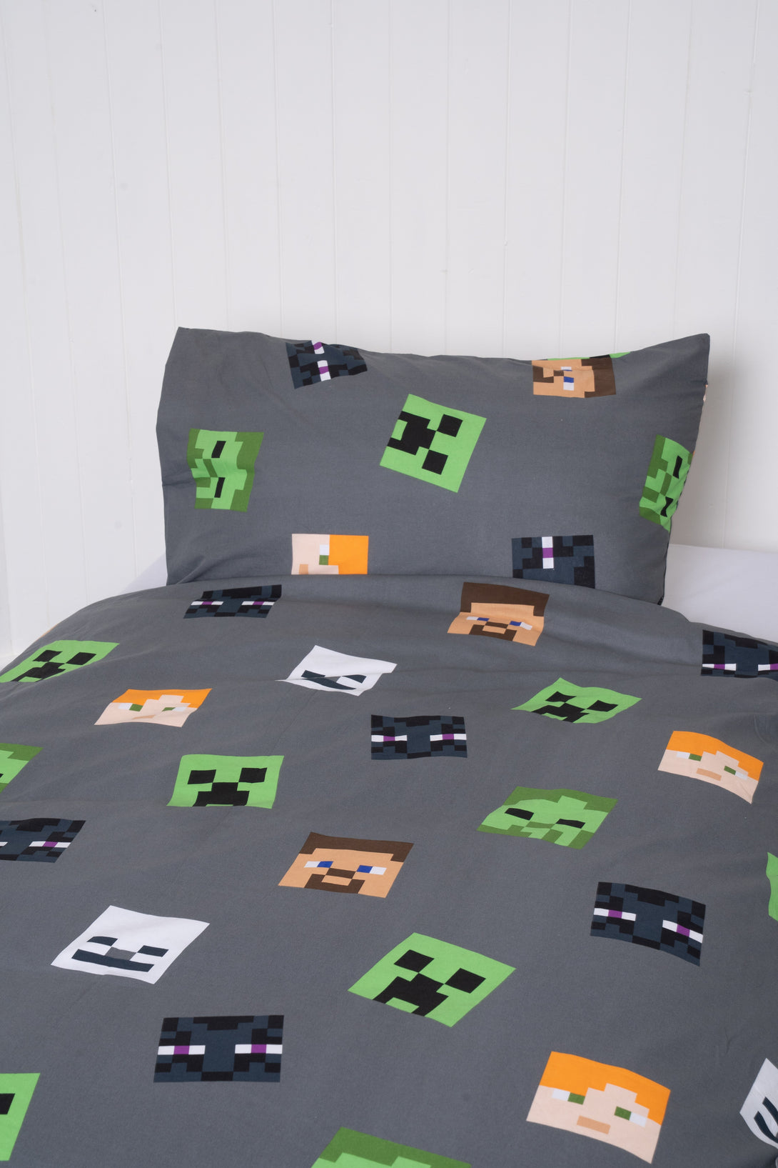 The BRIT DIAMOND Kids Minecraft Reversible Duvet Cover Set features colorful pixelated characters, like Creepers and Steve, for playful gamer bedroom decor. The double-sided bedding stands out against a plain white wall.
