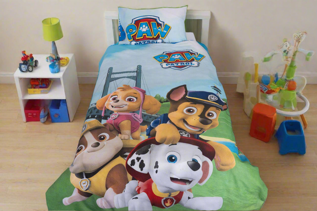 A children’s room features the BRIT DIAMOND Kids Paw Patrol Reversible Duvet Cover Set—2-in-1 Adventure Bedding for Little Heroes—with cartoon characters, a white nightstand, toys, lamp, and a playset with slide on a wooden floor.
