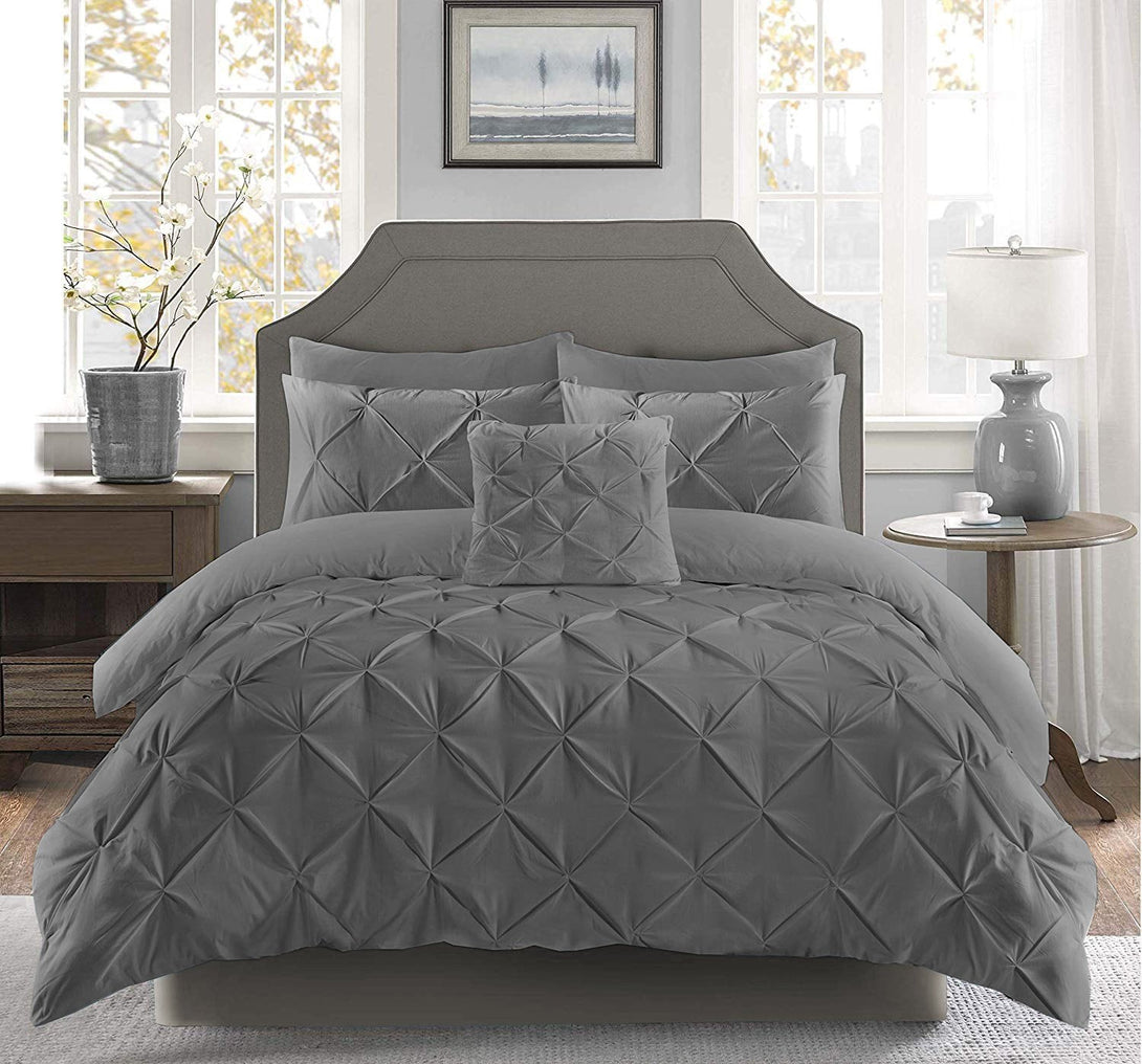 A bright bedroom features a neatly made bed adorned with the BRIT DIAMOND Pintuck Duvet Set, crafted from 100% Egyptian Cotton, along with matching pillows, two windows, a nightstand with lamp, potted plant, and framed artwork above the headboard.