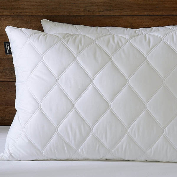 A close-up of two BRIT DIAMOND Luxury Pillow 2 Pack with quilted covers, featuring a diamond pattern, stacked on a bed with a wooden headboard—hotel quality soft down alternative pillows for all types of sleepers.