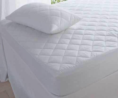 A neatly made bed features the BRIT DIAMOND Quilted Mattress Protector 100% Cotton, a diamond-patterned, anti-allergy fitted cover available in all UK sizes (30cm & 40cm extra deep), with natural light streaming in by the window.