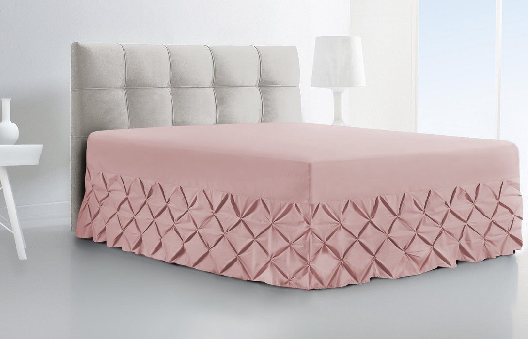 A modern bedroom showcases a neatly made bed with a tufted gray headboard and the BRIT DIAMOND Luxury Fitted Pintuck Valance Sheet, crafted from 100% Egyptian cotton, featuring a pink pleated diamond-patterned skirt.