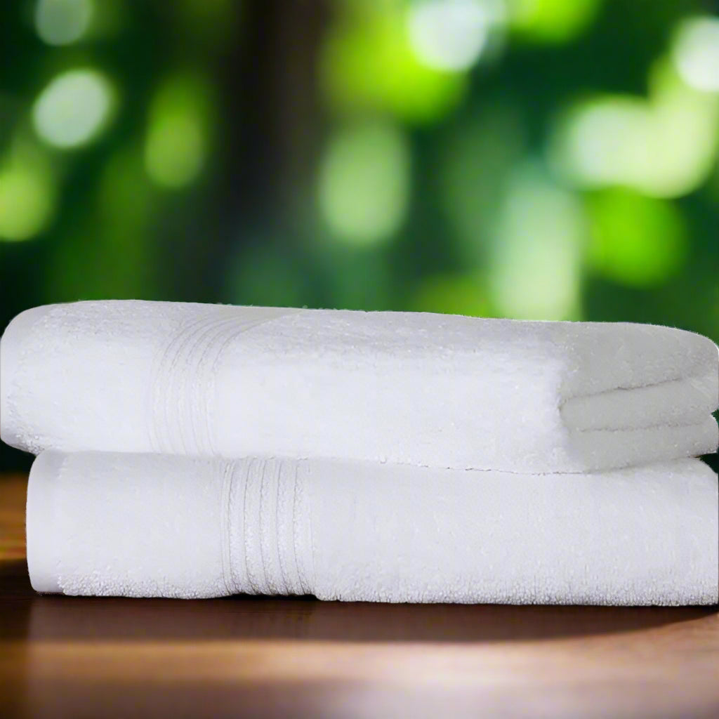 Two BRIT DIAMOND 100% cotton bath sheets, quick-dry and ultra soft, are neatly stacked on wood, with green plants and a white brick wall in the background. Ideal for spa, gym, guest, or bathroom. Pack of 2 premium towels.