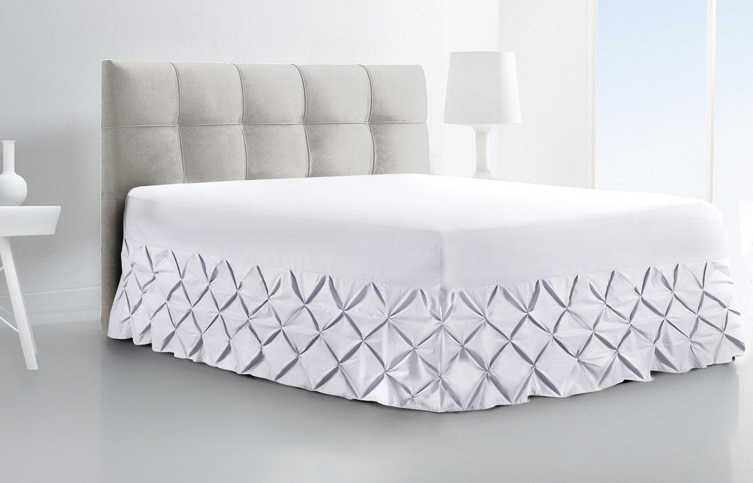 A modern, minimalist bedroom features a neatly made bed with the BRIT DIAMOND Luxury Fitted Pintuck Valance Sheet in 100% Egyptian Cotton, light gray tufted headboard, and crisp white decor.