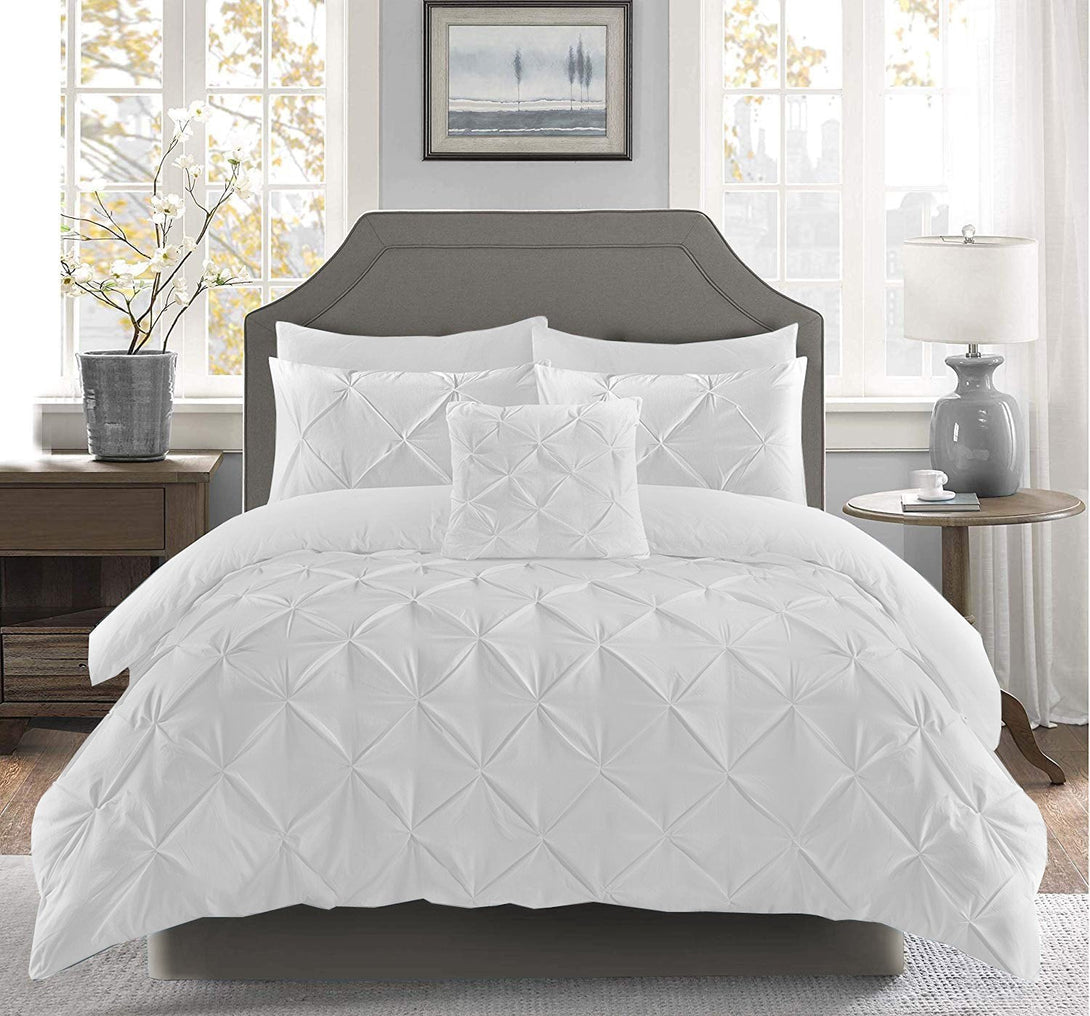 A bright bedroom features a neatly made bed with the BRIT DIAMOND Pintuck Duvet Set 100% Egyptian Cotton, textured white quilt cover and pillows, a gray upholstered headboard, potted plant, table lamp, and framed wall art above.