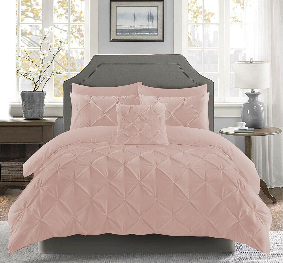 A bright bedroom features a neatly made bed with the BRIT DIAMOND Pintuck Duvet Set, 100% Egyptian Cotton, in light pink, alongside pillows, gray headboard, nightstands, a lamp, a vase with branches, and framed art.