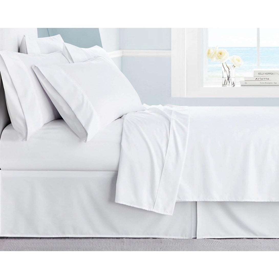 A neatly made bed with BRIT DIAMONDs Luxury Hotel Quality 400TC Extra Deep 40cm Fitted Sheet in 100% Egyptian Cotton sits by an ocean-view window, white flowers on the sill, and light blue and white walls complete the serene room.