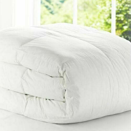A fluffy white BRIT DIAMOND Premium Hotel Quality Duvet Deep Sleep Quilt is neatly folded on a bed by a sunlit window, offering all UK sizes and togs 4.5–15 for custom comfort.